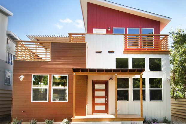 Modern two-story house with a mix of red, white, and wooden exterior finishes, featuring large windows and a front entrance with steps.