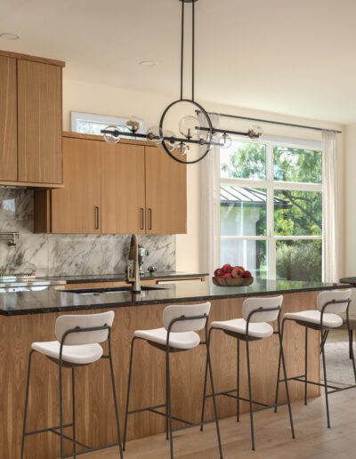 Modern kitchen and dining area with wooden cabinets, marble backsplash, black countertops, bar stools, round dining table, and large windows letting in natural light.