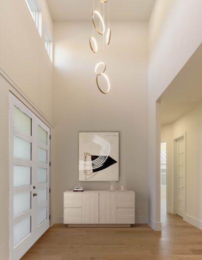 A modern entryway with light wood floors, a frosted glass front door, a white console table, abstract wall art, and a cluster of circular pendant lights hanging from the ceiling.